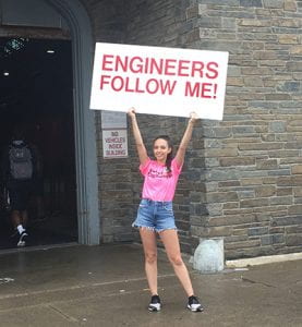 Photograph of a Cornell Engineering student holding a large sign over her head that reads, 